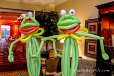 two balloons in the shape of frogs with eyes and arms, standing next to each other