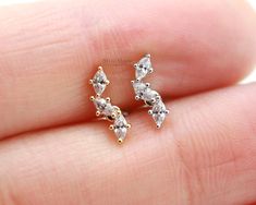 two small white diamond stud earrings on someone's finger