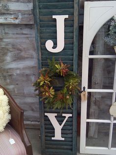 a door with a wreath and the word joy hanging on it's side next to a chair