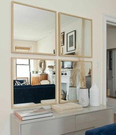 three mirrors are hanging on the wall above a dresser with books and vases in front of it