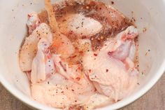 a white bowl filled with chicken and seasoning sitting on top of a wooden table