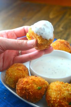 a person is holding up some fried food with ranch dressing on the side and dipping sauce in a small white bowl