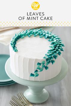 a white cake with blue frosting and green leaves on top, sitting on a plate