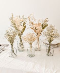 four glass vases filled with flowers on top of a white cloth covered tablecloth