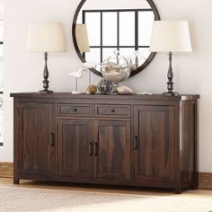 a wooden sideboard with two lamps and a round mirror