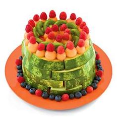 a large cake made out of fruit on top of an orange plate with berries and kiwis