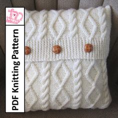 a white knitted pillow with buttons on the front and back of it, sitting on a couch