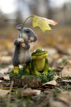 a toy mouse and frog are standing next to each other on the ground with leaves