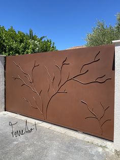 a metal gate with a tree design on the top and bottom part, in front of a concrete wall