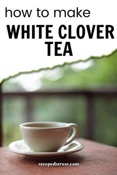 a white coffee cup sitting on top of a wooden table next to a green leafy tree