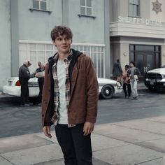 a young man standing on the sidewalk in front of a building with police cars behind him