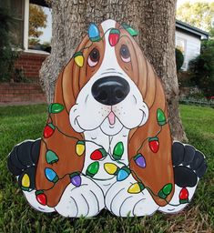 a brown and white dog with christmas lights on it's face sitting under a tree