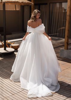 a woman in a white wedding dress standing on a wooden floor with her hands behind her back