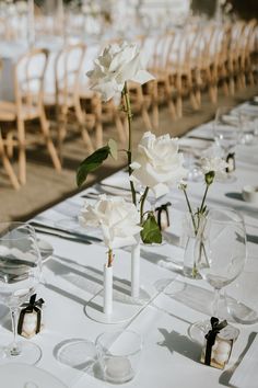 the table is set with white flowers in vases and empty wine glasses on it