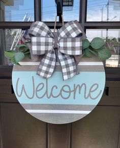 a welcome sign hanging on the front door of a house with plaid bow and greenery