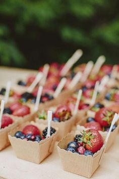 small cups with strawberries and blueberries on them sitting on a table in front of trees