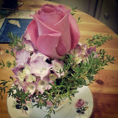 a pink rose sits on top of a white plate with greenery and flowers in it