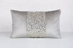 a grey pillow with silver sequins on the front and back, sitting against a white wall