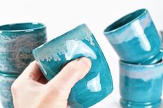 a hand is holding a blue mug in front of four other cups on a table