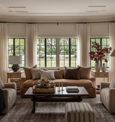 a living room filled with lots of furniture next to two large windows covered in curtains