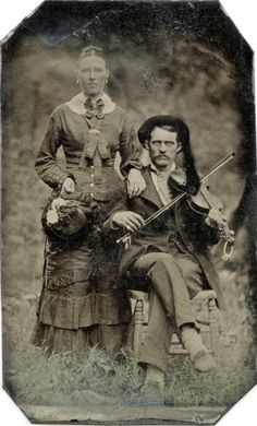 an old time photo of two people sitting on a chair with a violin in their hands