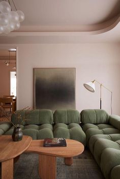 a living room filled with green couches and a wooden coffee table in front of a painting on the wall