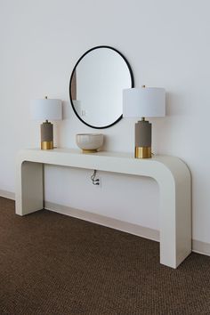 a white console with two lamps and a round mirror