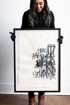 a woman holding up a black and white framed art piece with writing on the front