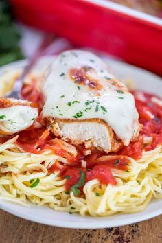 a white plate topped with pasta and meat covered in sauces on top of a wooden table