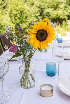 a sunflower is in a vase on a table with wine glasses and other place settings