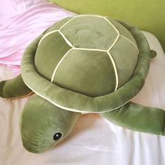 a stuffed turtle laying on top of a bed next to a pink pillow and blanket