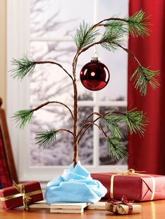 a small christmas tree sitting on top of a wooden table next to presents and a red ornament