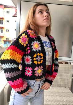 a woman standing in front of a tv wearing a colorful crocheted sweater and jeans