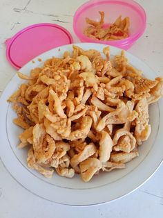 a white plate topped with fried food next to two pink plastic bowls filled with food