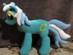 a crocheted blue pony sitting on top of a floor next to a wall