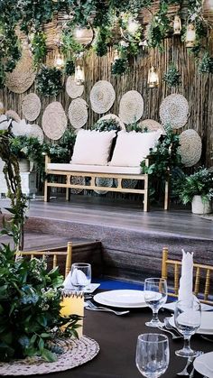 a set table with place settings and greenery on the wall behind it in front of a seating area