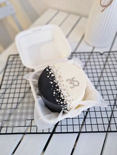 a black and white frosted donut in a box on a wire rack next to a cup