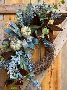 a wreath with blue flowers and greenery hanging on a wooden door frame in the shape of a heart