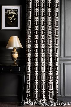 a black and white patterned curtain hanging in front of a table with a lamp on it