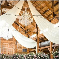 a chandelier hanging from the ceiling in a barn filled with flowers and greenery