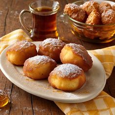 powdered sugar covered donuts on a plate next to a cup of tea and honey