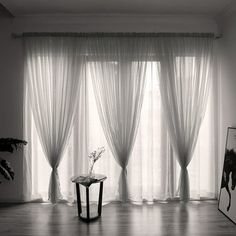 a black and white photo of a living room with sheer drapes on the windows