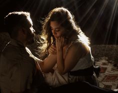 a man kneeling down next to a woman on top of a bed in the dark