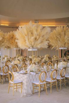 the tables are set with white and gold linens, tall centerpieces, and large feathers