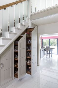 an open shoe cabinet under the stairs in a room with white walls and flooring