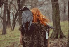 a woman walking in the woods with a bird on her back, and two crows perched on her shoulders