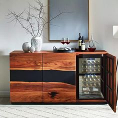 a wooden cabinet with wine bottles and glasses on it in front of a wall mounted mirror