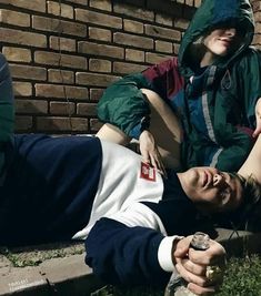 two people laying on the ground near a brick wall