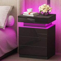 a night stand with flowers on it in front of a pink wall next to a bed