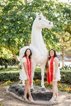 two women standing next to a white horse statue